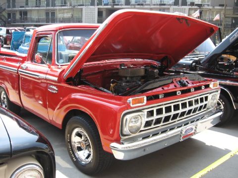 1966 Ford F-100 - A red Ford pickup truck is displayed with its hood open, revealing the engine compartment.