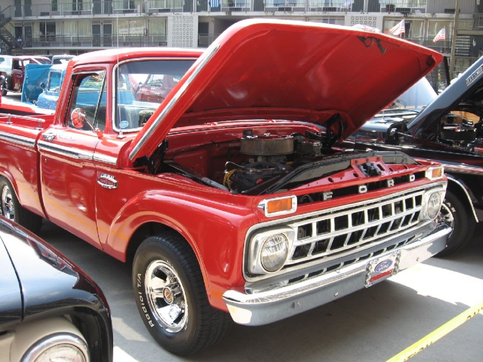 Red Ford pickup with hood open, showing engine. Parked next to other vehicles