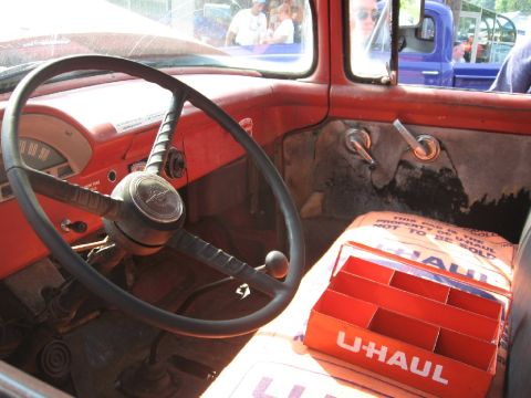 1966 Ford F-100 - The interior of a red 1966 Ford F-100 pickup truck features a U-Haul seat cover and an orange organizer on the passenger seat.