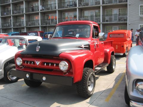 1966 Ford F-100 - A red pickup truck with a black hood and large tires is parked in a lot with other vehicles.