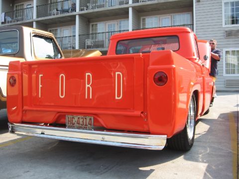 1966 Ford F-100 - Orange 1956 Ford F-100 pickup truck parked outdoors with a hotel in the background.