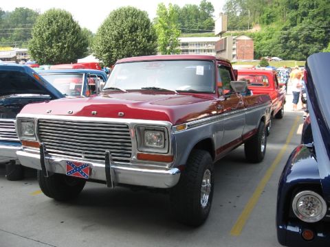 1966 Ford F-100 - A two-tone Ford F-Series truck is parked in a lot with other vehicles, displaying a decorative license plate.