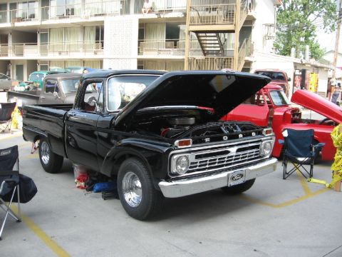 1966 Ford F-100 - A black Ford pickup truck is displayed with its hood open, parked alongside a red truck.