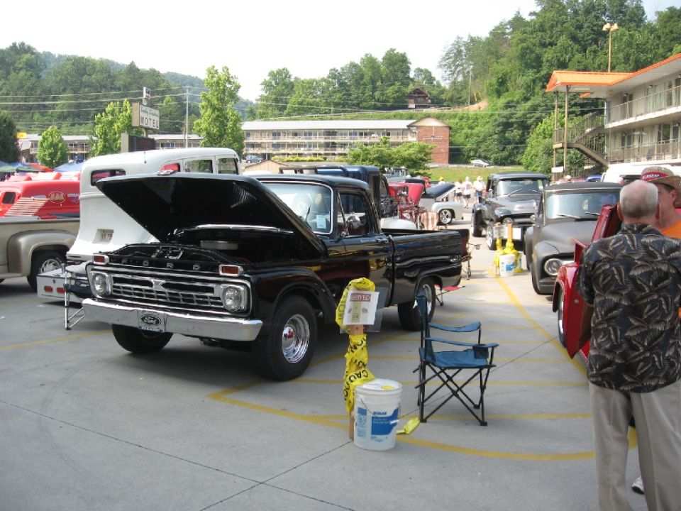 Black 1966 Ford F-100 pickup truck, hood open, parked at an outdoor event with other vehicles
