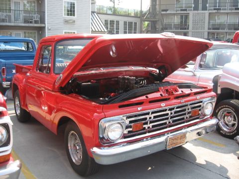 1966 Ford F-100 - A red 1965 Ford F-100 pickup truck is parked with its hood open, revealing the engine.