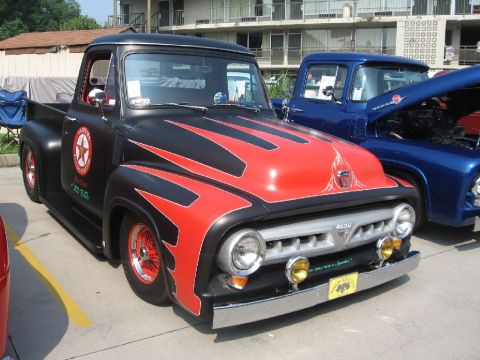 1966 Ford F-100 - Three-quarter front view of a slammed mid-1950s Ford F-100 pickup in satin black with red flame/scallop paint, red wire wheels, yellow fog…