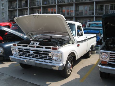 1966 Ford F-100 - A white 1965 Ford F-100 truck is displayed with its hood open, alongside other vehicles.