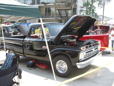 1966 Ford F-100 - A black 1966 Ford F-100 pickup truck is displayed with its hood open at an outdoor event.