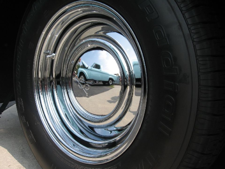 Chrome hubcap reflecting a light blue pickup truck with hood up