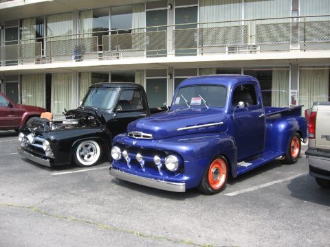 1966 Ford F-100 - Two classic Ford F-series pickup trucks, a blue 1951 and a black 1950s model, are parked in front of a motel.