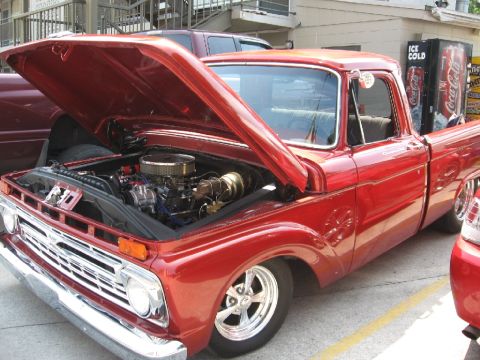 1966 Ford F-100 - A red pickup truck is parked with its hood open, revealing the engine bay. Another vehicle is partially visible in the foreground.