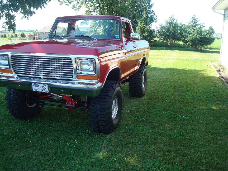 Lifted red 1970s Ford 4x4 on mud tires parked on a green lawn