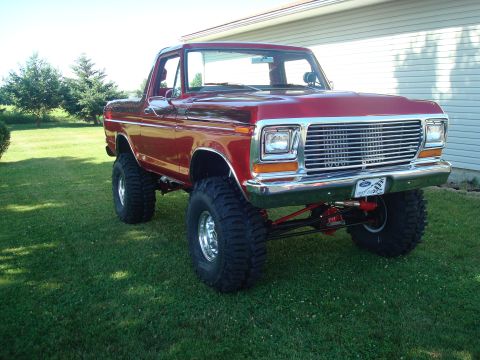 1978 Ford Bronco - This red 1978 Ford Bronco features a lifted suspension and oversized tires, parked on a grassy lawn.