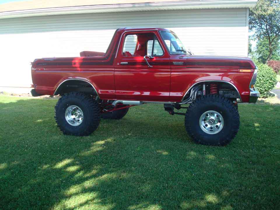 Lifted red topless Ford Bronco on polished wheels and mud tires parked on grass