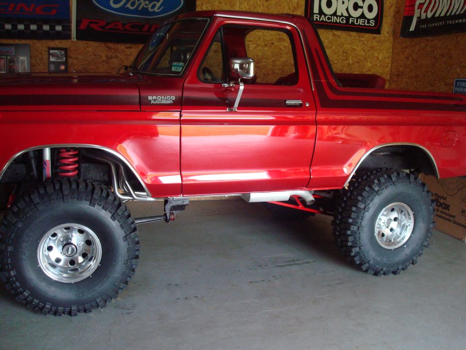 Lifted red Ford Bronco Ranger side profile with mud tires, aluminum wheels and side exhaust