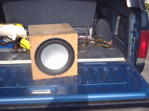 1990 Ford Bronco - A subwoofer box sits in the bed of a blue pickup truck, with wiring and other items visible.