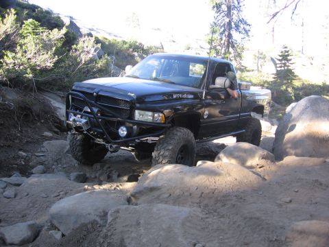 1989 Ford Bronco - A black pickup truck with "WT4x4" badging is shown off-roading on a rocky terrain.