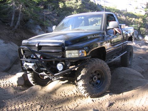 1989 Ford Bronco - A black pickup truck modified for off-roading navigates a rocky, sandy trail.