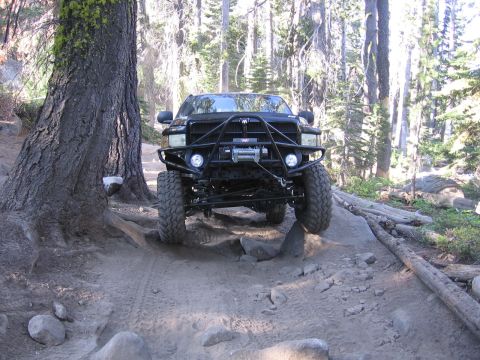 1989 Ford Bronco - A modified pickup truck navigates a rocky trail through a dense forest.