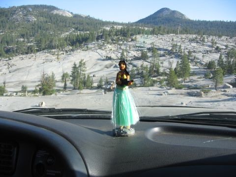 1989 Ford Bronco - Dashboard view with a hula dancer figurine, overlooking a rocky, tree-covered mountain landscape.