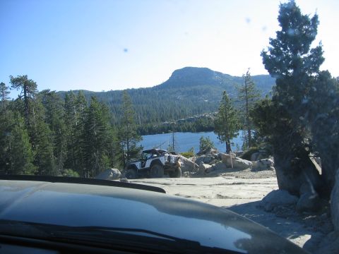 1989 Ford Bronco - A white off-road vehicle is parked on a rocky area next to a lake, with a forested mountain range behind it.