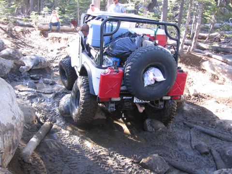 1989 Ford Bronco - An off-road vehicle traverses a challenging, muddy, and rocky terrain with its occupants and supplies onboard.
