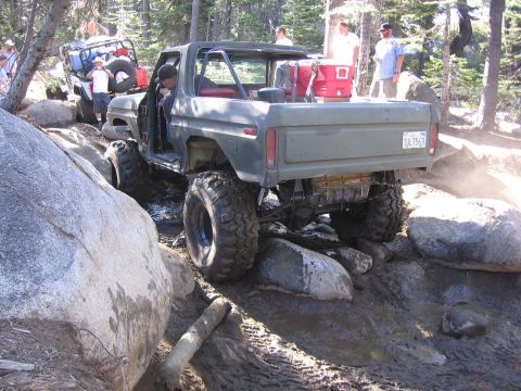 1989 Ford Bronco - Off-road truck with custom roll cage and large tires navigating a difficult rocky trail.