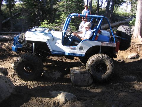 1989 Ford Bronco - An off-road vehicle with a roll cage is shown traversing a challenging, rocky trail.