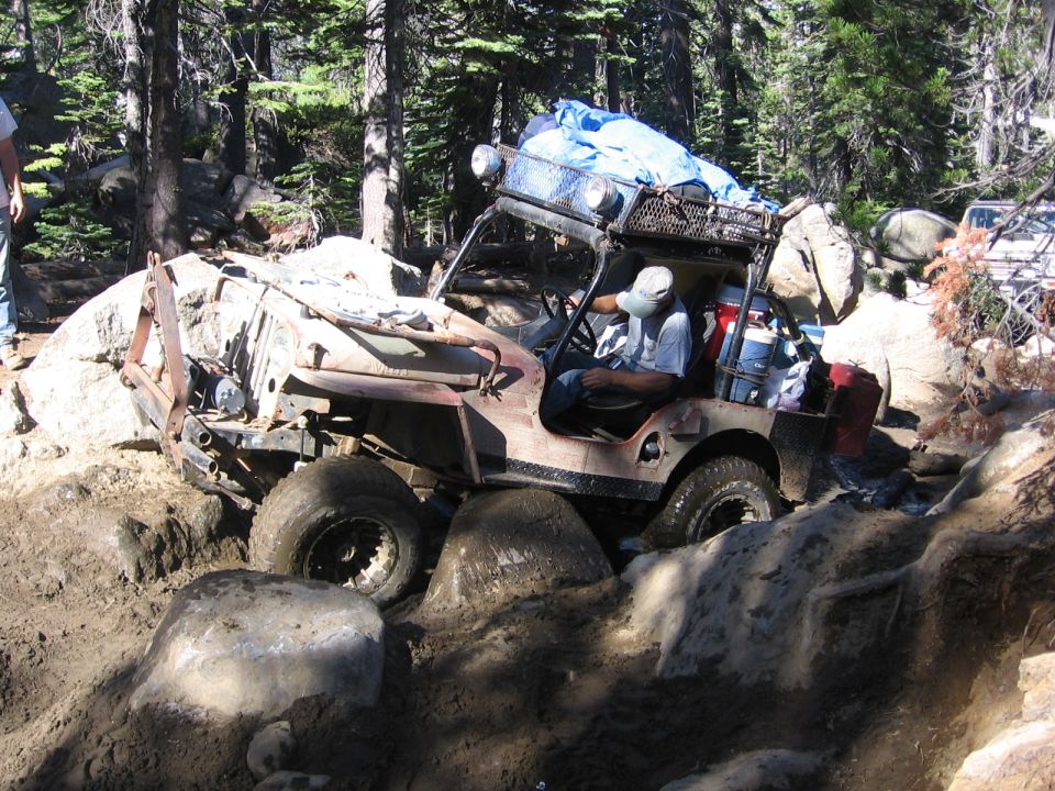 Modified off-road vehicle stuck on rocks and mud with a person inside
