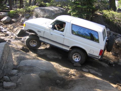 1989 Ford Bronco - A white 1989 Ford Bronco navigates a rocky off-road trail with its tires on large boulders.