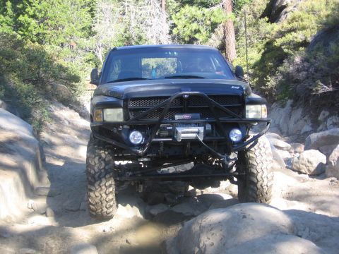 1989 Ford Bronco - A black truck with a custom bumper and winch drives over rocks on a dirt path.