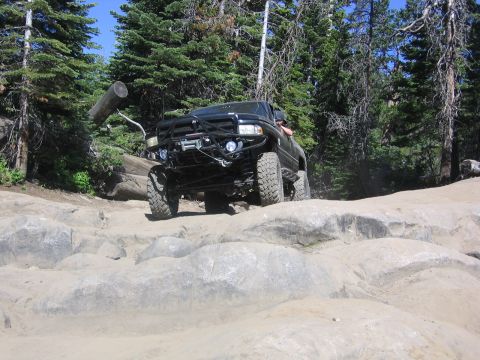 1989 Ford Bronco - A black off-road truck navigates a rocky trail surrounded by trees.