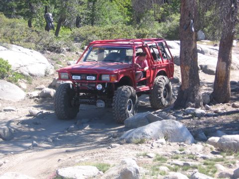 1989 Ford Bronco - This heavily modified off-road vehicle navigates a rocky, wooded terrain.