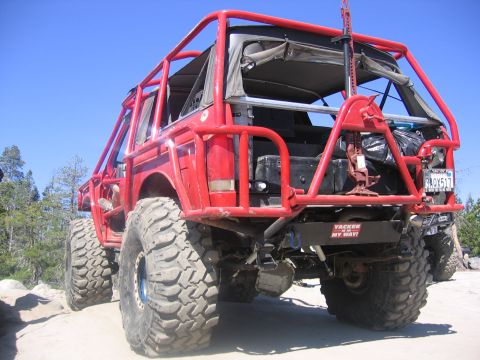 1989 Ford Bronco - Modified off-road vehicle with extensive roll cage and large tires seen from the rear.