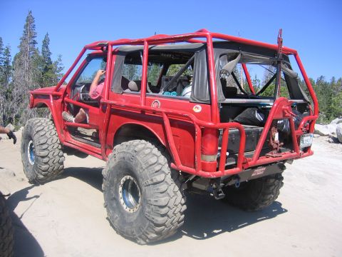1989 Ford Bronco - Modified off-road vehicle with custom roll cage and oversized tires on a rocky trail.
