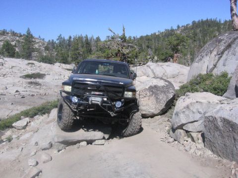 1989 Ford Bronco - A modified pickup truck is shown navigating a challenging rocky terrain with large boulders on either side.