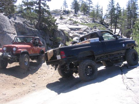 1989 Ford Bronco - Two off-road vehicles navigate a challenging rocky path in a wooded, mountainous area.