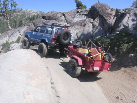1989 Ford Bronco - Off-roading scene with a blue Jeep Cherokee towing a trailer up a rocky, dirt path.