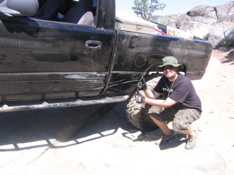 1989 Ford Bronco - A man poses next to a heavily scratched black pickup truck, highlighting its off-road capabilities and damage.