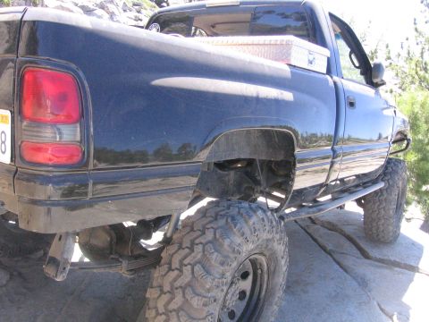 1989 Ford Bronco - A black pickup truck with large off-road tires is parked on rocks, with a toolbox visible in the bed.