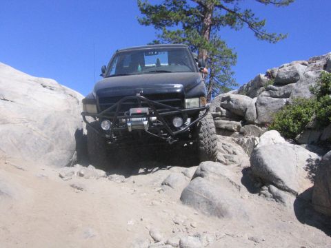 1989 Ford Bronco - A black truck is shown navigating a challenging rocky terrain under a clear blue sky.