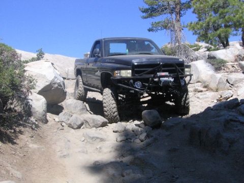 1989 Ford Bronco - Modified black pickup truck tackles a challenging rocky off-road course under a clear blue sky.