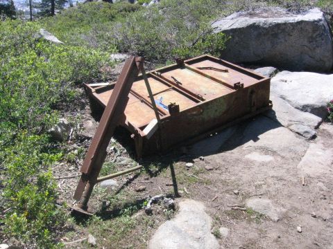 1989 Ford Bronco - A derelict metal container sits abandoned in a rocky, vegetated outdoor area.