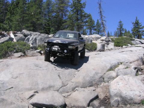 1989 Ford Bronco - A black pickup truck navigates a challenging rocky terrain under a clear blue sky.