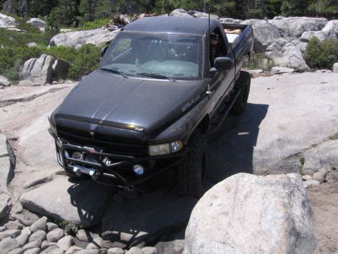 1989 Ford Bronco - This black pickup truck is equipped for off-roading, with a winch and large tires visible as it traverses a rocky landscape.