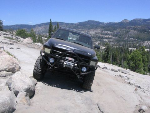 1989 Ford Bronco - Off-road truck navigates a challenging rocky path with a mountainous landscape in the background.
