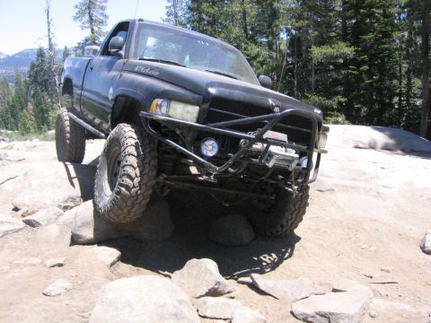 1989 Ford Bronco - Modified black Dodge Ram pickup truck climbing over rocks on a trail.