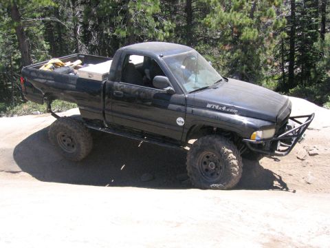 1989 Ford Bronco - A black pickup truck navigates a challenging off-road terrain with its tires angled on the dirt.
