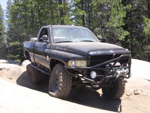 1989 Ford Bronco - This modified black pickup truck navigates a challenging off-road trail with large tires and a custom bumper.