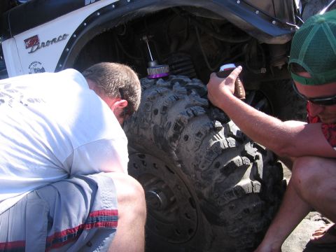 1989 Ford Bronco - Two people inspect the tire and suspension of a white 1989 Ford Bronco.
